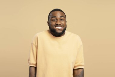 Neşeli bir Afro-Amerikan 'ın stüdyo portresi. Günlük kıyafetler giymiş komik bir surat yapıyor ve bej bir arka planda gülümsüyor.