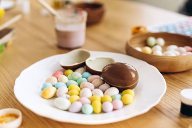 Paskalya yumurtaları ve beyaz tabakta renkli şekerler. Ahşap masada Paskalya kutlaması için dekore ediliyor. Gelenek kavramı