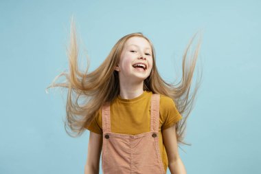 Paskalya için saçını sallayan ve mavi arka planda gülen neşeli bir kızın stüdyo portresi.