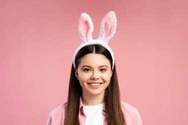 Tavşan kulaklığı takan neşeli genç kızın stüdyo portresi, gülümseyen ve paskalya veya bahar şenliklerini pembe arka planda kutlayan. Kutlama konsepti
