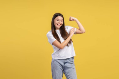 Neşeli genç kız kaslarını esnetiyor ve gücünü gösteriyor, canlı sarı bir arka plana karşı güç ve vücut pozitifliğini arttırıyor. Spor konsepti
