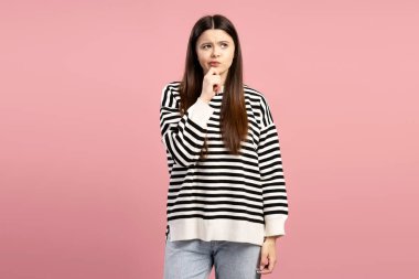 Bir karar verirken çenesine dokunan düşünceli genç bir kızın, canlı pembe bir arkaplana karşı düşünceli bir yüz ifadesi sergilediği bir stüdyo fotoğrafı. Reklam kavramı