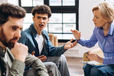 Psikolog muayenehanesinde terapi seansı sırasında babasına bağıran genç bir çocuk. Aile sorunları, gençlik sorunları, terapist, tavsiye, yardım kavramı