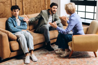 Ofiste psikologla konuşurken babasının bağırıp oğlunu işaret ettiği portre. Aile sorunları, gençlik sorunları, terapist, tavsiye, yardım kavramı