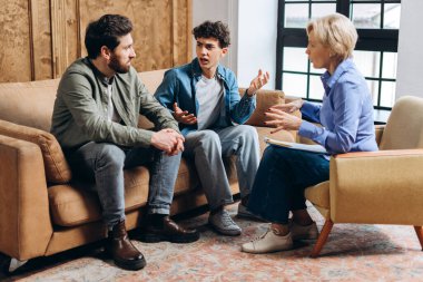 Stresli genç çocuk, kadın psikolog ve babasıyla olan sorunundan bahsediyor. Aile sorunları, gençlik sorunları, terapist, tavsiye, yardım kavramı