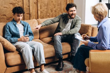 Öfkeli baba ve psikoterapistin portresi terapi seansı sırasında oğlunun duyguları hakkında konuşuyor. Aile sorunları, gençlik sorunları, terapist, tavsiye, yardım kavramı