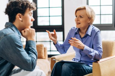 Orta yaşlı kadın psikolog ofiste genç bir çocukla konuşuyor. Psikolojik destek kavramı