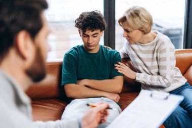 Psikolog notlar yazarken genç oğlunu sakinleştiren üzgün kadının portresi. Danışmanlık terapisi. Psikoloji tedavisi