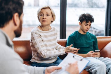 Anne portresi, genç oğlu ve telefon bağımlılığı hakkında erkek psikologla konuşuyor. Danışmanlık terapisi. Psikoloji tedavisi