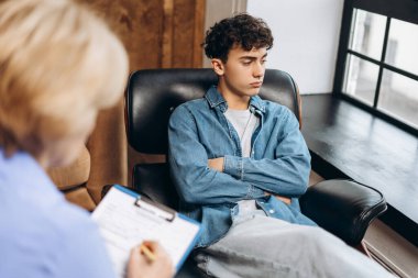 Ofiste terapi seansı sırasında ellerini çapraz yapıp psikoterapist dinleyen üzgün genç bir çocuğun portresi. Ruh sağlığı konsepti