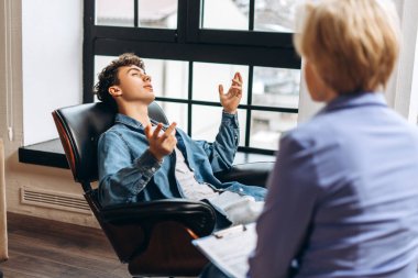 Genç bir çocuğun portresi sandalyede oturuyor, terapi sırasında kadın psikologla konuşuyor. Ruh sağlığı konsepti
