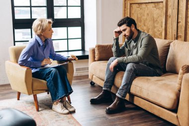 Ofisteki psikoterapistle randevusu sırasında koltukta oturan elleri başının yanında olan depresyondaki bir adam. Bir psikoloğun yardımı