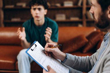 Genç çocuğu dinlerken not yazan sakallı profesyonel erkek psikanalistin portresi. Danışmanlık terapisi. Psikoloji tedavisi