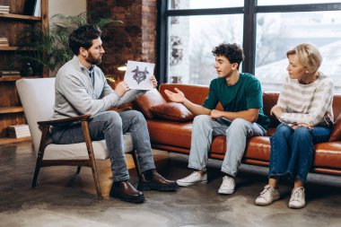 Yetişkin erkek psikoloğun portresi genç hasta ve annesine muayenehanede tıbbi test sonuçlarını gösteriyor. Danışmanlık terapisi. Psikoloji tedavisi