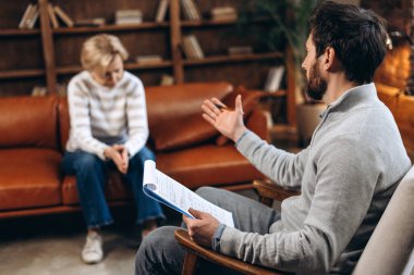Heyecanlı kadın portresi erkek psikologla terapi seansı yapıyor, elinde bir not panosu, konuşuyor. Psikolojik destek kavramı
