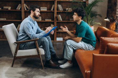 Profesyonel psikoloğun genç bir çocukla konuşurken not defterine not aldığı bir kenar görüşü. Psikoterapi hizmetleri, ruhsal sağlık profesyonel konsepti