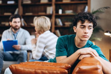 Annesinin ofiste erkek psikologla konuşmasını bekleyen üzgün genç bir çocuk. Danışmanlık terapisi. Psikoloji tedavisi