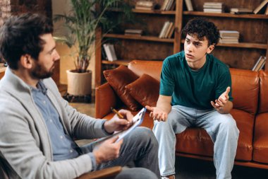 Profesyonel orta yaşlı erkek psikoloğun portresi genç bir çocukla konuşan notlar yazıyor. Danışmanlık terapisi. Psikoloji tedavisi