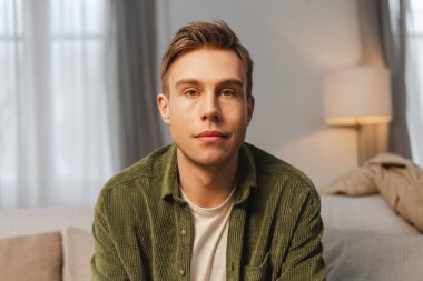 Oturma odasındaki rahat koltukta oturan ve kameraya bakan ciddi bir gencin portresi. Reklam kavramı