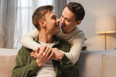 Mutlu eşcinsel çift, evde rahat bir kanepede kucaklaşan iki pozitif erkek. İlişki, aşk kavramı