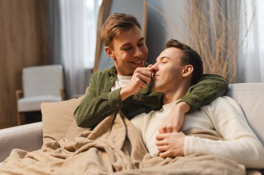 Mutlu eşcinsel çift, sarılan iki adam evde rahat bir kanepede battaniye örtüyor. Aşk, ilişki kavramı