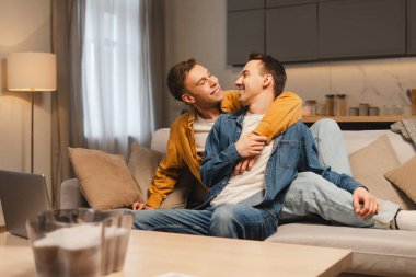 Gülümseyen, çekici eşcinsel çift gündelik kıyafetler giyip evdeki oturma odasında rahat bir kanepede dinleniyorlar. Aşk, ilişki kavramı