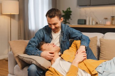 Mutlu eşcinsel çift kanepede dinleniyor ve evde birlikte vakit geçiriyorlar rahat bir kanepeye oturup sarılıyorlar. Aşk, ilişki kavramı