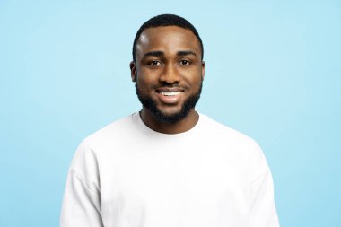 Beyaz tişört giyen genç Afro-Amerikan bir portre, geniş bir mavi arka plan karşısında gülümsüyor, mutluluk ve pozitiflik saçıyor. Reklam kavramı