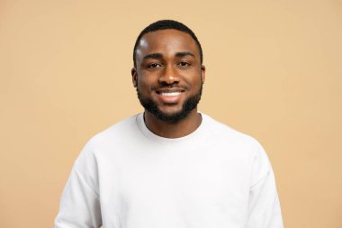Beyaz kazak giyen, bej bir arka plana özgüven ve pozitiflik saçan neşeli, Afro-Amerikan bir adamın stüdyo portresi. Reklam kavramı