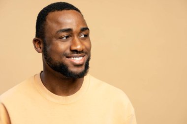 Neşeli Afro-Amerikalı adam bej bir süveter giyiyor, nazikçe gülümsüyor ve bej bir arka plana bakıyor, pozitiflik saçıyor, kopyalama alanı. Reklam kavramı