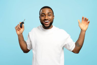 Mutlu bir Afrikalı genç adam araba anahtarı tutuyor ve neşeli bir ifadeyle kutluyor. Yeni bir araç almanın heyecanını ve neşesini gösteriyor. Ya da ehliyetini alıyor.