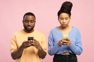 Genç Afro-Amerikalı kadın ve erkek, akıllı telefonlarını canlı pembe bir arka plan üzerinde odaklanmış olarak kullanıyorlar, modern iletişim ve dijital bağlılık sergiliyorlar.