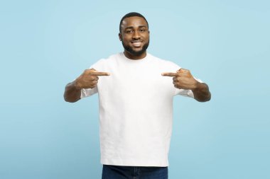 Beyaz tişörtünü gösteren neşeli bir Afro-Amerikalı 'nın stüdyo portresi, canlı mavi bir arkaplan karşısında metin ve tasarımlar için özelleştirilebilir bir alan sunuyor. Reklam kavramı