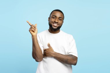 İşaret parmağıyla mavi arka planda izole edilmiş ilginç bir şeyi işaret eden Afro-Amerikalı genç bir yetişkinin stüdyo portresi. Alışveriş konsepti