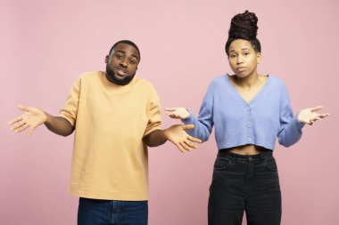 Afro-Amerikalı erkek ve kadın, ne bileyim, kafası karışık bir yüz ifadesiyle el kaldırıyorlar, ne olup bittiği hakkında hiçbir fikirleri yok, pembe arka planda duruyorlar. Hareketli kavram