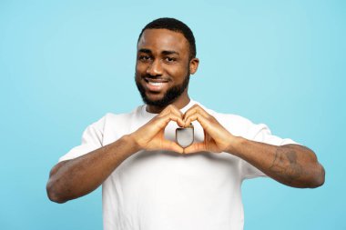 Mutlu Afrikalı Amerikalı bir adam, elleri bir akıllı yamağın etrafında, canlı mavi bir arka plan karşısında, teknolojiye ve bağlantıya olan sevgisini ifade ederek kalp şekli oluşturuyor. Sağlık hizmeti kavramı