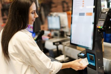 Modern kadın müşteri süpermarkette kasiyerlik yapıyor, teknolojinin rahatlığını kucaklarken kusursuz ve verimli bir alışveriş deneyimi yaşıyor.