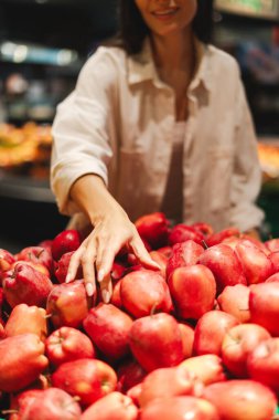 Müşteri marketten taze meyve seçiyor, olgun meyvelerden kırmızı elma topluyor, sağlıklı alışveriş deneyimlerinin tadını çıkarıyor.
