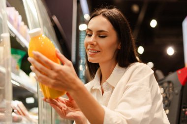 Mutlu müşteri, çekici Latin kadın gülümserken marketin soğutulmuş bölümünden taze portakal suyu seçiyor canlı renklerin ve sağlıklı seçeneklerin tadını çıkarıyor.