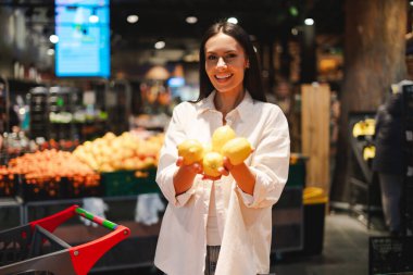 Mutlu müşteri, yanında alışveriş arabası olan markette alışveriş yaparken limon gösteren Latin bir kadın sağlıklı yemek seçeneklerinin tadını çıkarıyor. Alışveriş konsepti