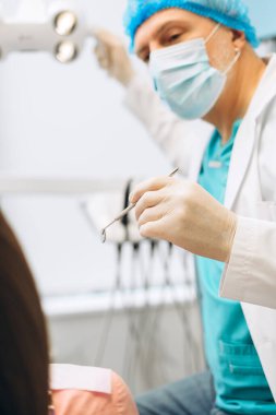 Diş sağlığı kliniğinde aletlerle kadın hastayı muayene eden koruyucu maskeli yetişkin erkek dişçinin portresi. Diş sağlığı, sağlık hizmetleri konsepti