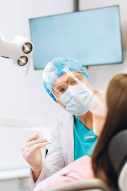 Koruyucu tıbbi maske takmış profesyonel yetişkin erkek dişçinin portresi. Ofisinde kadın hastaların dişlerini inceliyor. Sağlık hizmetleri diş tedavisi