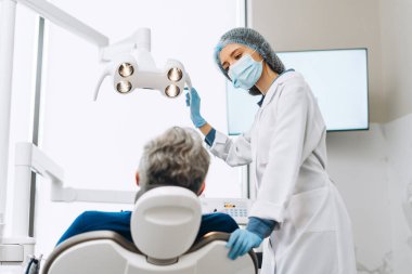 Diş muayenehanesindeki erkek hasta için diş lambası kullanan üniformalı profesyonel bir bayan doktor. Sağlık hizmetleri diş tedavisi