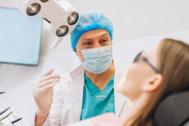 Profesyonel erkek dişçi portresi. Klinikteki genç kadın hastaya diş kontrolü yapmak için kullanılıyor. Diş sağlığı, sağlık hizmetleri konsepti