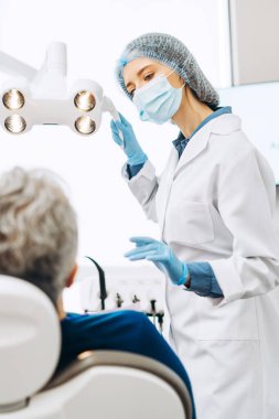 Koruyucu yüz maskesi takan kadın dişçi portresi olgun bir adam için diş muayenesine hazırlanıyor. Sağlık hizmetleri diş tedavisi