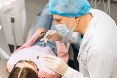 Profesyonel yetişkin erkek dişçinin portresi koruyucu gözlüklü kadın patentinin dişlerini kontrol ediyor. Diş sağlığı, sağlık hizmetleri konsepti