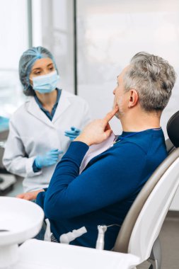 Diş sağlığı kliniğindeki randevusu sırasında kadın diş hekimi ile konuşan olgun bir adamın portresi. Sağlık hizmetleri diş tedavisi