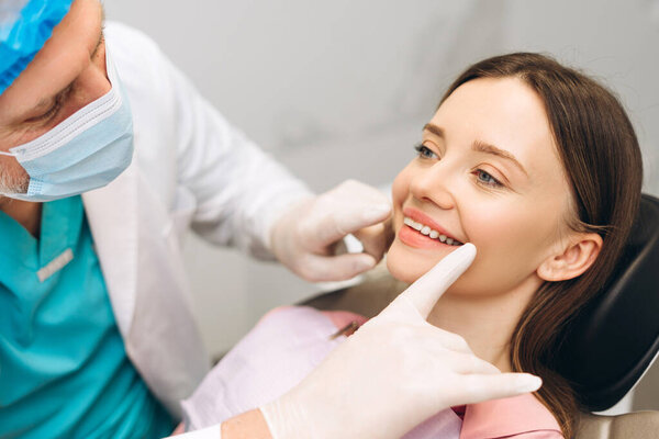 Портрет мужчины-дантиста в маске для лица, осматривающего своего прекрасного пациента в кабинете дантиста. Здравоохранение