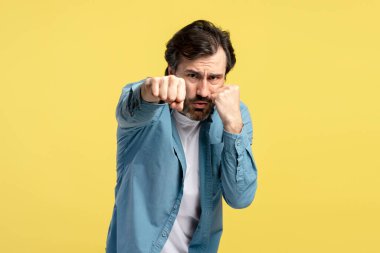 Stüdyo çekimlerinde sakallı, mavi tişörtlü, güçlü yumruklar atan güçlü sarı arka plan, güç, kararlılık ve yoğun odaklanma gösteren bir adam vardı.