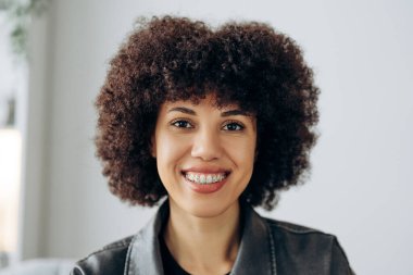 Afro-Amerikalı genç bir kadının portresi, diş telleri ve şehvetli bir afro saç stili ile özgüven içinde gülümseyen eşsiz güzelliğini ve ortodontik tedavisini sergiliyor. Diş sağlığı konsepti